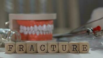 Word FRACTURE composed of wooden dices. Pills, documents, pen, human jaw model in the background. photo