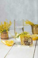 Glass of water, honeycomb, two pieces of lemon. Mimosa flowers in background. photo