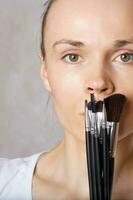 Young lady keeps make up brushes kit close to her face. Closeup photo