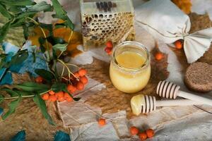 serbal bayas, vaso con miel y panal en un arpillera. . foto