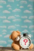 Question mark depicted on a vintage clock with academic cap. Brown plush teddy bear in the background. photo