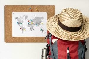 Planning Travel destination concept. Corkboard with world map and pins on wall, backpack and summer hat photo