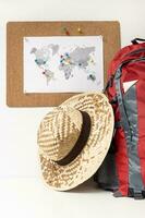 planificación viaje destino concepto. tablero de corcho con mundo mapa y patas en muro, mochila y verano sombrero foto