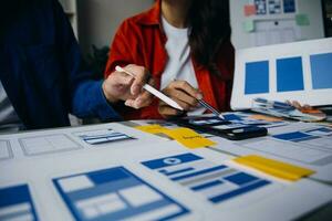 Close up ux developer and ui designer brainstorming about mobile app interface wireframe design on table with customer breif and color code at modern office.Creative digital development agency photo