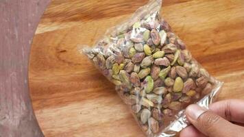 Putting packet of pistachios nuts a wooden board on gray background video