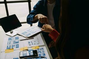 Close up ux developer and ui designer brainstorming about mobile app interface wireframe design on table with customer breif and color code at modern office.Creative digital development agency photo
