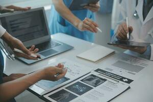 Multiracial team of doctors discussing a patient standing grouped in the foyer looking at a tablet computer, close up view photo