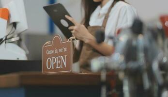 Welcome. Open. barista, waitress woman turning open sign board on glass door in modern cafe coffee shop ready to service, cafe restaurant, retail store, small business owner, food and drink concept photo