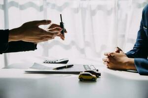 A car rental company employee is handing out the car keys to the renter after discussing the rental details and conditions together with the renter signing a car rental agreement. Concept car rental. photo