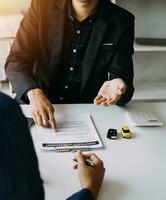 A car rental company employee is handing out the car keys to the renter after discussing the rental details and conditions together with the renter signing a car rental agreement. Concept car rental. photo