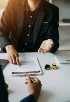 A car rental company employee is handing out the car keys to the renter after discussing the rental details and conditions together with the renter signing a car rental agreement. Concept car rental. photo