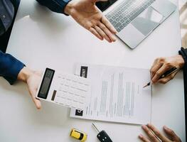 A car rental company employee is handing out the car keys to the renter after discussing the rental details and conditions together with the renter signing a car rental agreement. Concept car rental. photo