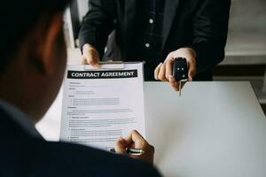 A car rental company employee is handing out the car keys to the renter after discussing the rental details and conditions together with the renter signing a car rental agreement. Concept car rental. photo