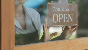 Young entrepreneur holding open sign on glass door at cafe photo