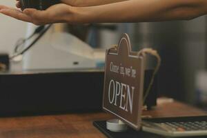 Young entrepreneur holding open sign on glass door at cafe photo