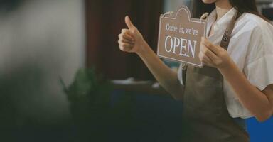 Young entrepreneur holding open sign on glass door at cafe photo