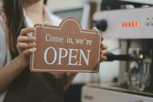 Young entrepreneur holding open sign on glass door at cafe photo