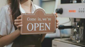 Young entrepreneur holding open sign on glass door at cafe photo