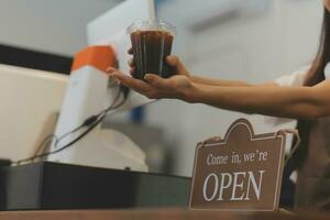 Bienvenido. abierto. barista, camarera mujer torneado abierto firmar tablero en vaso puerta en moderno café café tienda Listo a servicio, café restaurante, Al por menor almacenar, pequeño negocio dueño, comida y bebida concepto foto