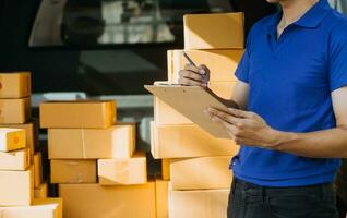 Delivery man with cardboard box checking document list In van and parcels on seat outside the warehouse. photo