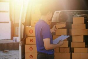 Delivery man with cardboard box checking document list In van and parcels on seat outside the warehouse. photo