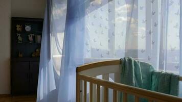 Empty baby boy room. Turquoise color fabric beside the bed. Blue transparent curtains at decorated window in the background video