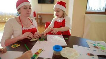 Young mother between 25 and 30 years old is painting with her children at round table in living room. Christmas period vacation video