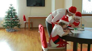 Young mother between 25 and 30 years old is painting with her children at round table in living room. Christmas period vacation video