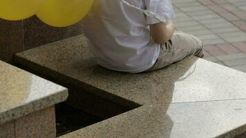traurig Junge von Sieben Jahre alt mit Geburtstag Luftballons ist warten zum jemand. Junge hat ein Geburtstag Papier Hut auf seine Kopf video