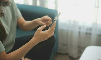 Happy Asian teen girl holding pad computer gadget using digital tablet technology sitting on the couch at home. Smiling young woman using apps, shopping online, reading news, browsing internet on sofa photo