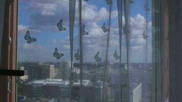Weiß transparent voile ist hängend beim breit Fenster dekoriert durch Papier Schmetterlinge mit Stadt Aussicht hinter das Vorhang video