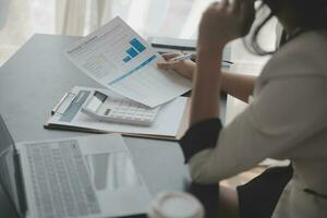 Asian Business woman using calculator and laptop for doing math finance on an office desk, tax, report, accounting, statistics, and analytical research concept photo