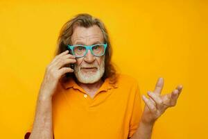 retrato de contento mayor hombre vistiendo azul lentes amarillo camisa hablando en el teléfono amarillo antecedentes foto