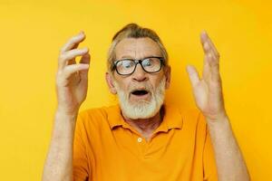 Senior grey-haired man posing yellow tshirt glasses yellow background photo