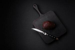 Fresh, ripe, soft brown colored avocado on a dark concrete background photo