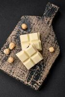 delicioso dulce blanco chocolate roto dentro cubitos en un de madera corte tablero foto