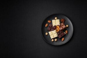 A mix of several types of delicious sweet chocolate broken into cubes on a black plate photo