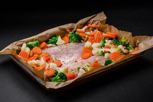 Raw sea bass fish fillet with salt, spices and vegetables in a baking dish photo