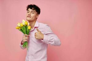 A young man in a pink shirt with a bouquet of flowers gesturing with his hands isolated background unaltered photo