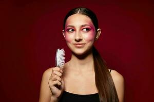 joven hermosa mujer con un peine en mano brillante maquillaje posando Moda emociones rosado antecedentes inalterado foto