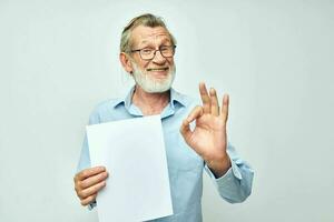 antiguo hombre en un azul camisa y lentes un blanco sábana de papel ligero antecedentes foto