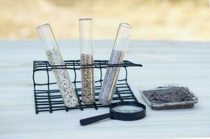 Test glass tubes that contain sample of different soil. Magnifying glass. Concept, soil quality inspection, research and science experiment. Find the best from different soil type and sources. photo