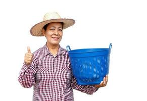 Happy senior Asian woman farmer wears hat, plaid shirt, thumbs up and holds blue empty basket. Smile . Concept, Agriculture occupation.  Thai farmer. photo