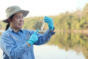 una investigadora ambiental asiática sostiene un tubo de agua de muestra para inspeccionar desde el lago. concepto, exploración, análisis de la calidad del agua de fuente natural. Investigación de campo en ecología. foto