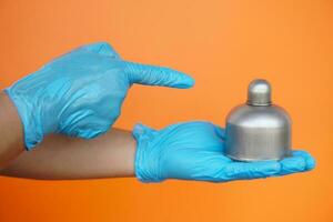 Close up  hands wears blue gloves point to alcohol burner  which used in laboratory , isolated on orange background. Concept, tool for doing science experiment. photo