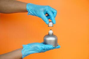 Close up  hands wears blue gloves hold alcohol burner  which used in laboratory , isolated on orange background. Concept, tool for doing science experiment. photo