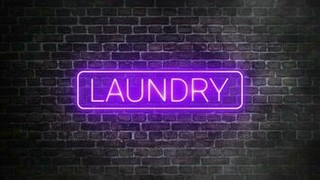 Laundry neon signboard on bricks wall background. Concept of laundry store front. Illuminated laundry word with rounded rectangle frame in purple neon color. video