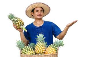 asiático hombre granjero usa sombrero, azul camisa, sostiene piña fruta. hacer mano gesto a presente producto. concepto , agricultura cosecha en tailandia granjero satisfecho. orgánico cultivos. estacional frutas foto