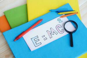 Paper card of formula EMC2 on colorful books with pen, crayons and magnifying glass. Concept, Einstein formula. Mass Energy Equivalence. Education, physics subject. photo