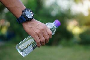 cerca arriba hombre mano sostener el plastico botella de agua, exterior. concepto, Bebiendo agua para salud, sano estilo de vida. temple sed, reducir fatiga, actualizar cuerpo. foto